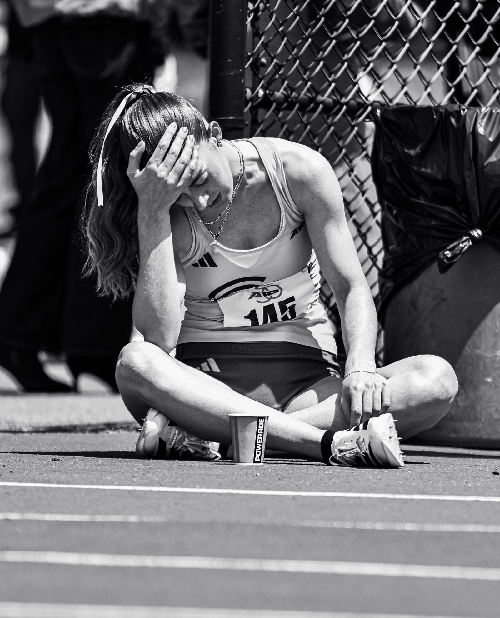 Black-and-white portrait of a George Mason track athlete sitting on the track after a race, head in hand.