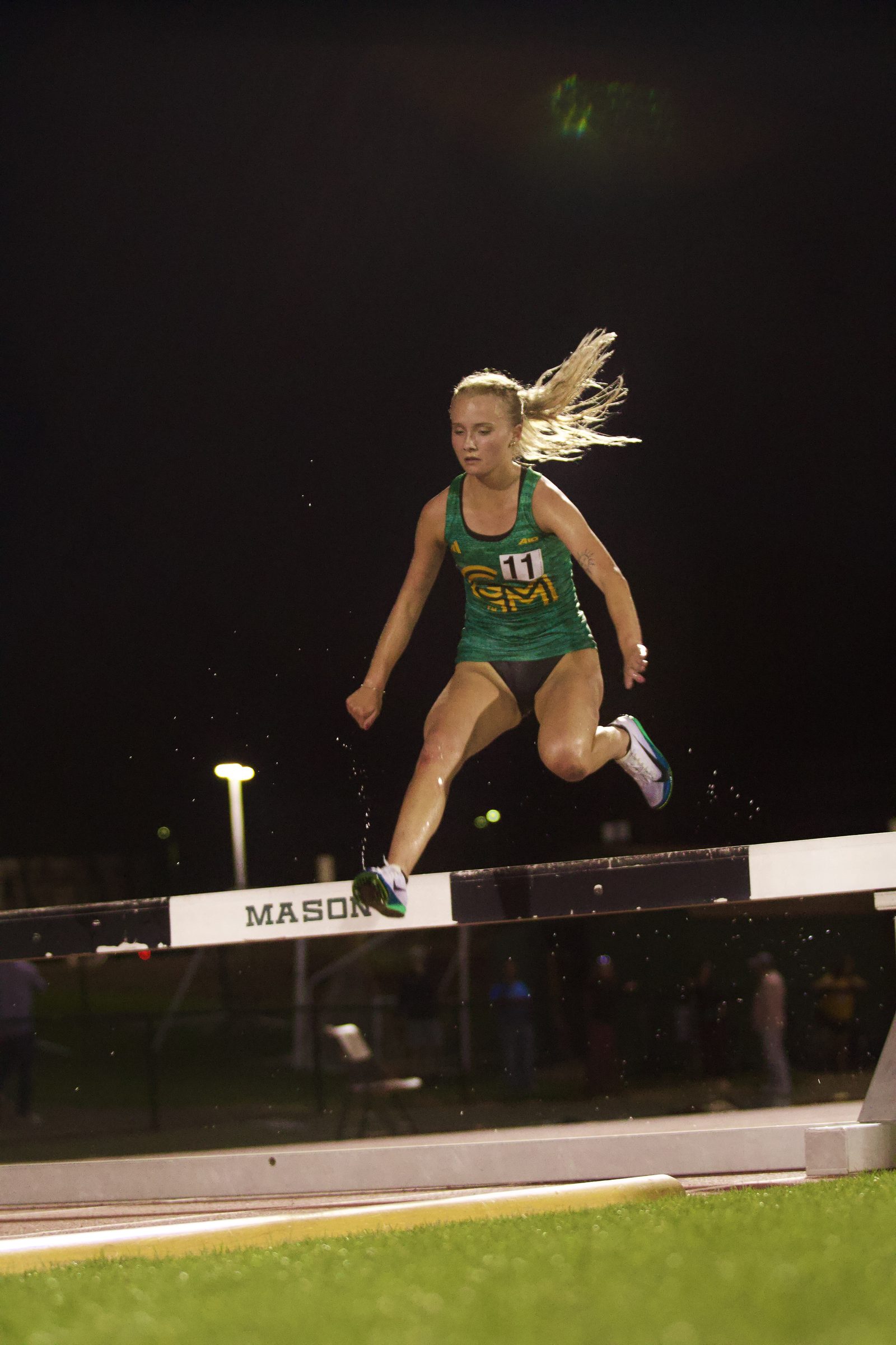 Steeplechase runner hurdles barrier under the lights.