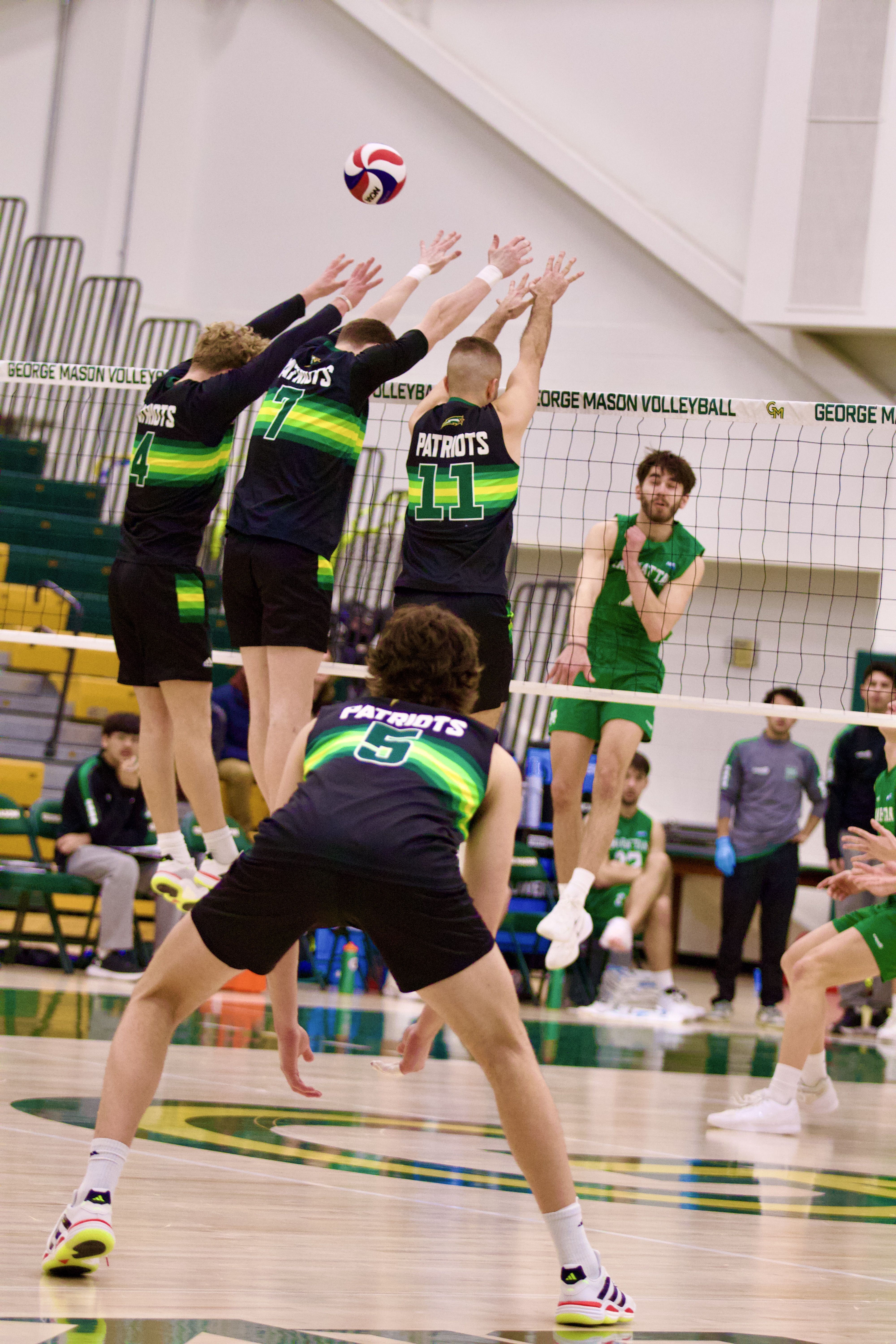 Teammates jump in sync to block spike from the opposing team. 